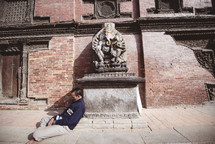 man sleeping leaning against a statue 