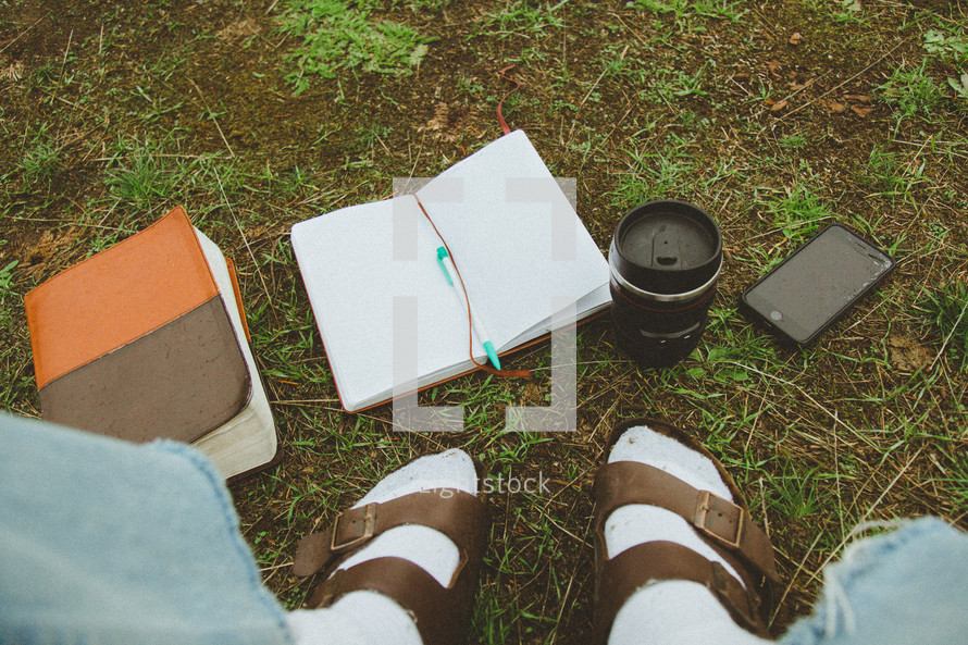feet in socks and sandals near a Bible, notebook, and coffee cup 