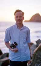 a man holding a camera by a shore 