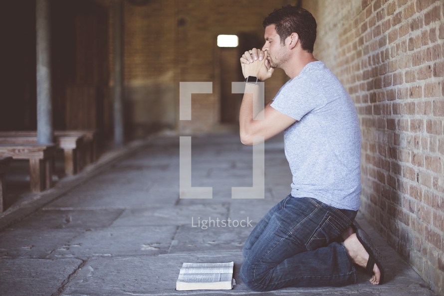 a man kneeling in prayer in front of a Bible 