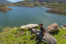 a girl sitting on a rock by a lake 
