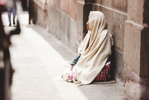 homeless woman siting on a sidewalk 