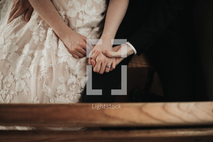 bride and groom holding hands sitting in a pew 