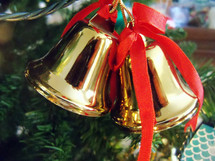 A set of Brass colored Christmas Bell Tree Ornaments adorned with red ribbons lighting up a  Christmas tree.