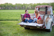 a couple sitting on the tailgate of a truck on a date 