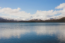 Clouds over snow-covered mountains surrounding a lake. 