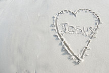 The word "Jesus" inside a heart drawn in the sand.