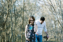 an expecting couple walking through a forest 