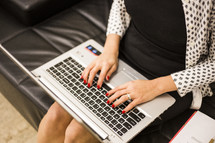 a woman sitting on a couch typing on a laptop 