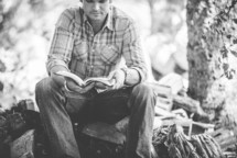 man reading a Bible next to pile of firewood 