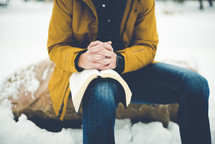 man sitting outdoors reading a Bible in winter 