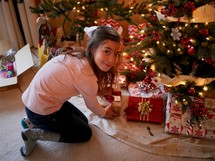 a girl looking at gifts under a Christmas tree 