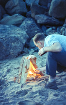 a man lighting a fire on a beach 