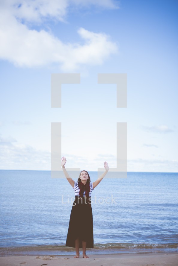 woman with hands raised praising God on a beach 