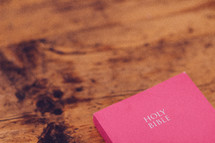 A bright pink Bible on a wooden surface.