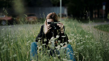 a young woman in tall grass holding a camera 