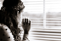 teen girl looking out window blinds 