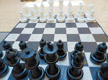 A black and white image of a huge chess board with chess pieces in black and white on a checkered black and white chess board that takes up about 10 feet of floor space symbolizing the game of life, life and death, good and evil, risk and chance and strategy and planning. All the things that make up life and thinking through moves that we make that can affect our spiritual and physical as well as mental well being. 

I saw this huge chess board at a local shopping mall and it just captured my imagination and had to photograph it. It reminded me of the game of life and the choices we have to make to affect our future as well as the spiritual battle between good and evil that we deal with in this life and the next. 