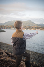 a boy child standing on a shore pointing out over the water 
