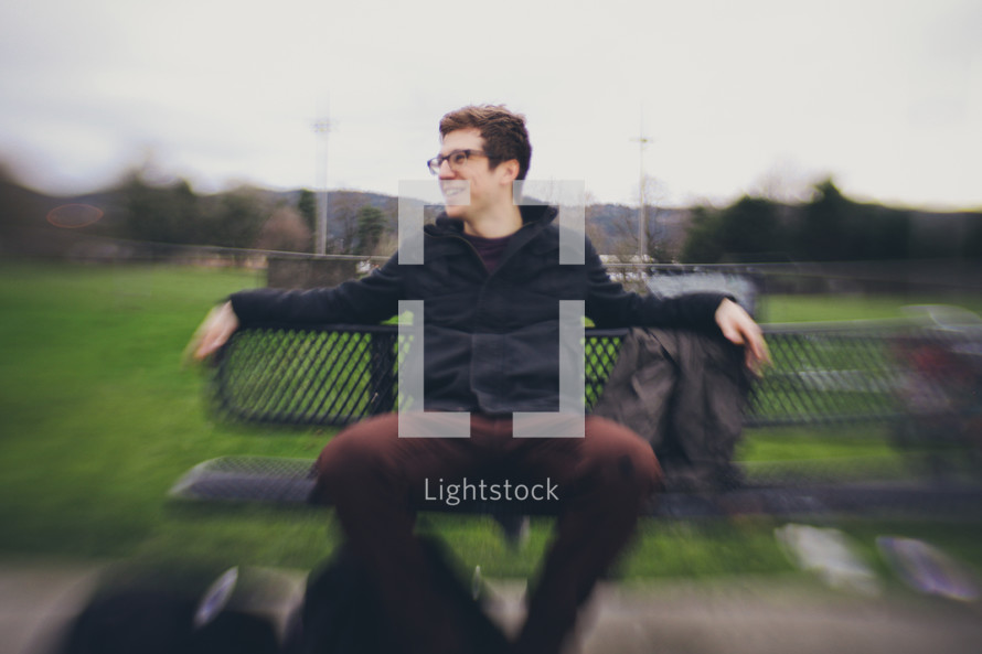 Bokeh image of man sitting on a park bench outside.