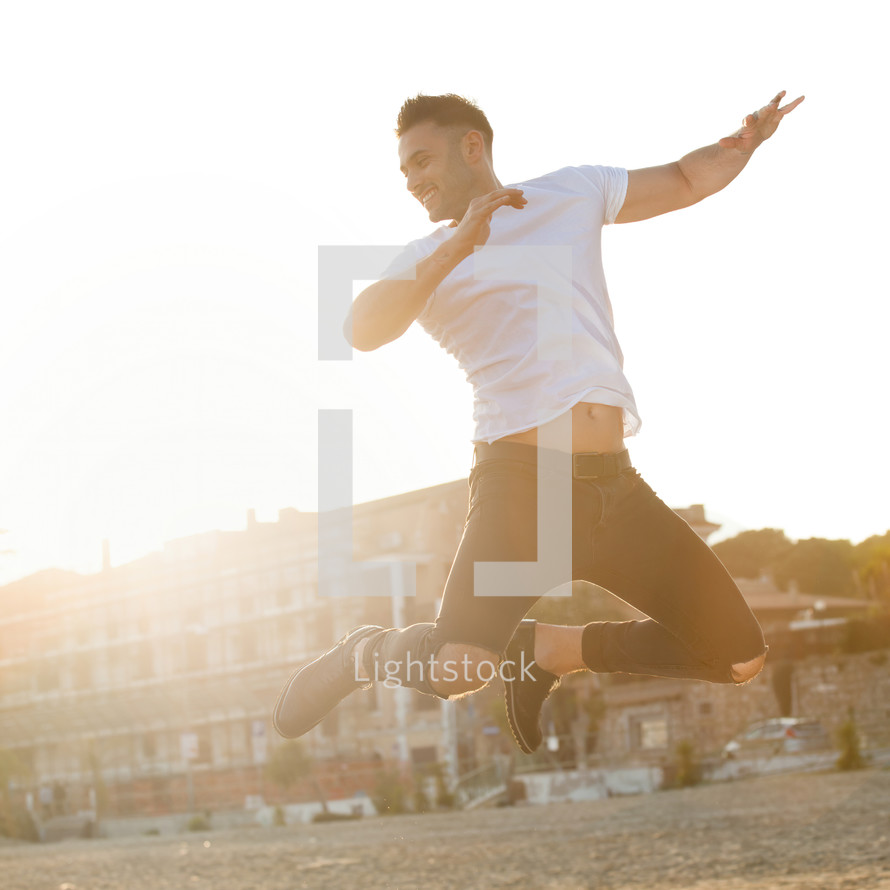 Portrait at sunset of a young man jumping with energy.