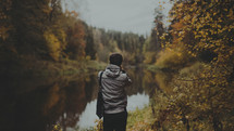 a man taking a picture of a pond in fall 