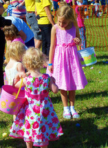 Three blonde haired girls with Easter baskets and Easter Dresses go on an Easter Egg hunt at a local  church ground for Easter. 