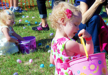 Two young sisters fill their baskets with Easter Eggs at a local outdoor church Easter Egg hunt for kids of all ages for Easter. 