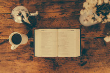 A Bible open to Proverbs and a cup of coffee on a rustic wooden surface.
