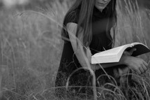 Woman reading Bible outdoors in an open field
