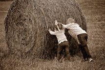 Children pushing a bail of hay