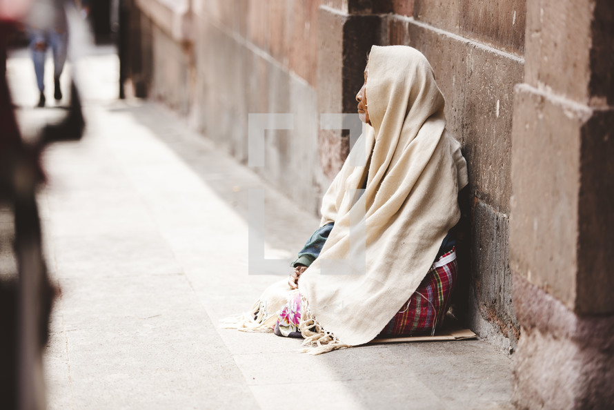 homeless woman siting on a sidewalk 
