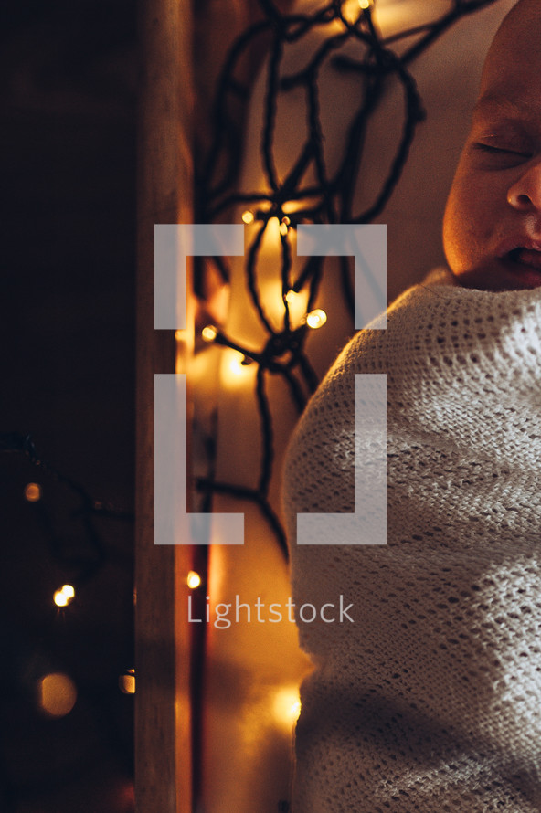 swaddled baby surrounded by Christmas lights 