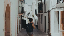 a woman with a backpack standing on a narrow street between buildings 