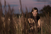 a woman in a field behind the blades of wheat grass