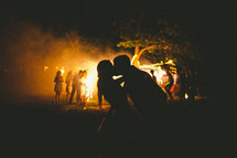 Silhouette of couple kissing by a campfire.