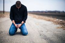 man kneeling on a road praying