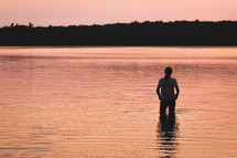 a woman standing in lake water at sunset 