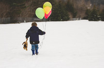 boy child walking in snow holding a teddy bear and balloons 