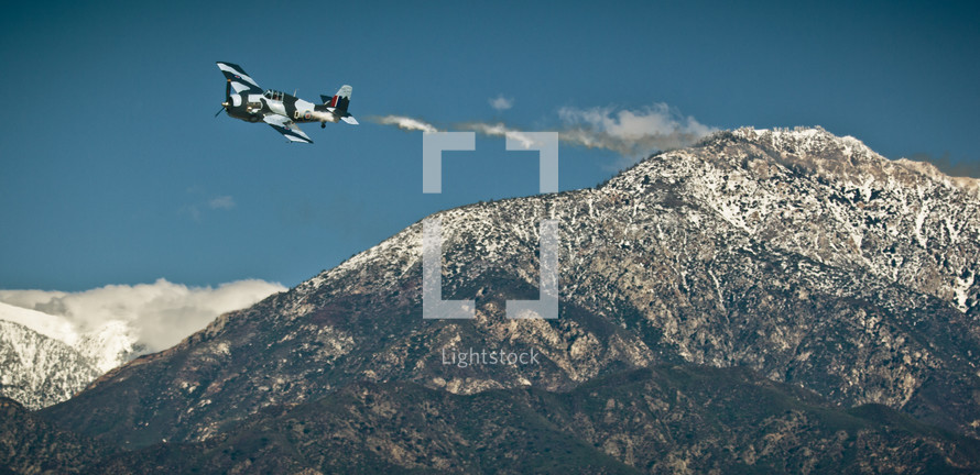 vintage single engine aircraft flying over mountains 