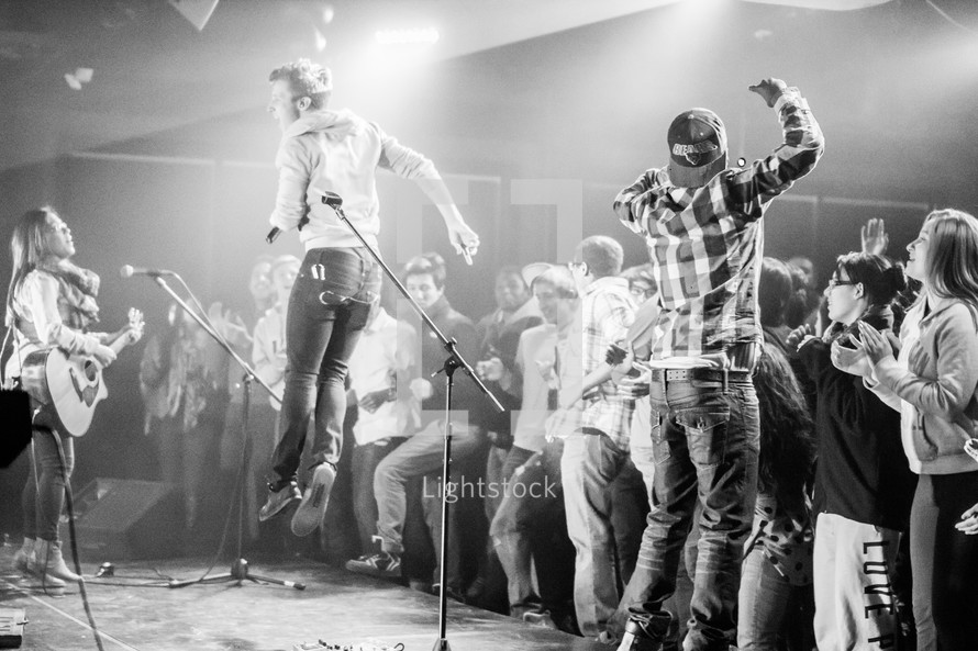 Audience rushing the stage during a concert with band jumping and playing.