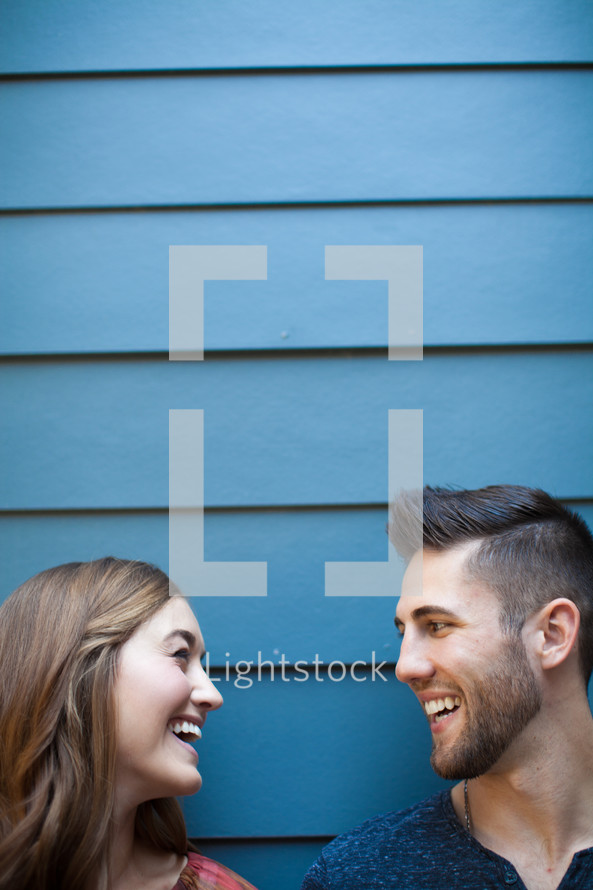 A man and woman smiling at each other against a blue wall.