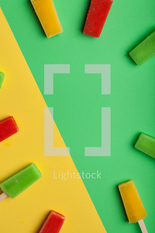 Brightly colored popsicles in a circle on green and yellow background.