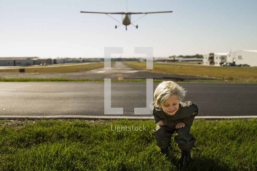 a boy child ducking as a plane flies over a runway