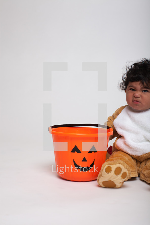 a toddler boy in a Halloween costume with a jack-o-lantern bucket 