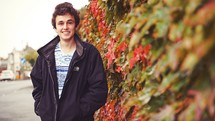 portrait of a teen boy standing near a wall covered in ivy