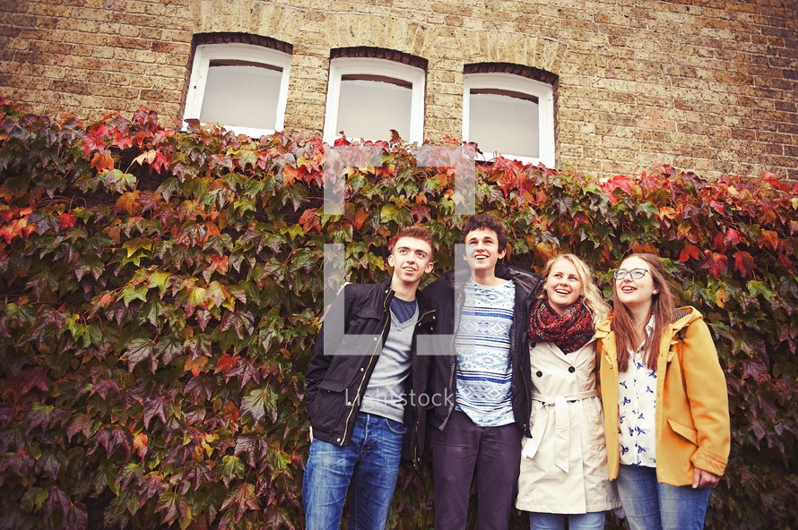 youth in coats standing in front a wall covered in ivy 