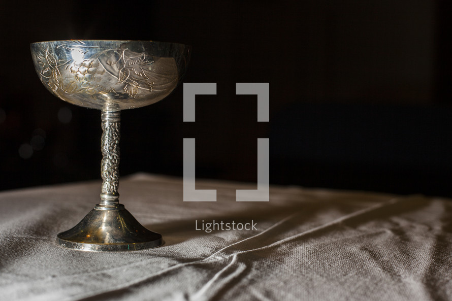 Silver chalice sitting on table top with table cloth.