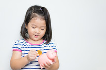  a little girl putting a coin in a piggy bank 