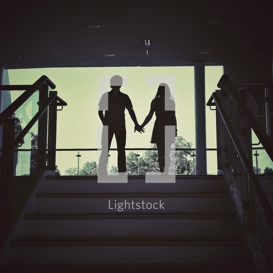 Silhouette of boy and girl holding hands at top of stair case.